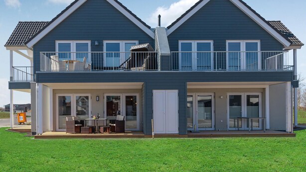 A two-story house with a balcony on the upper floor, a covered patio on the ground floor, and a garage door. - Gorgeous apartment in Büsum with sauna (Büsum)