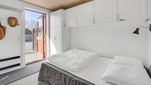 Ein Schlafzimmer mit einem Bett, weißen Schränken, einer Tür, die nach draußen führt, und einer kleinen Wandleuchte.
