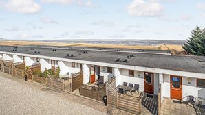 Eine Reihe weißer Gebäude mit nummerierten Türen, einer flachen Dachterrasse und Blick aufs Meer.