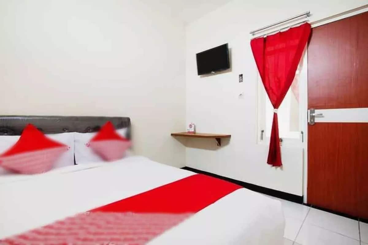 A hotel room with a bed, a TV mounted on the wall, and a door with a red curtain.