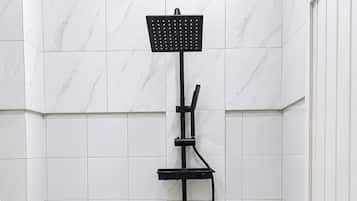 Et badeværelse med toilet i hvidt, bruseenhed i sort og flisebeklædte vægge.