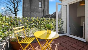 Eine kleine Außenpatio mit einem gelben Tisch und Stuhl, umgeben von Topfpflanzen und Blick auf ein Gebäude.