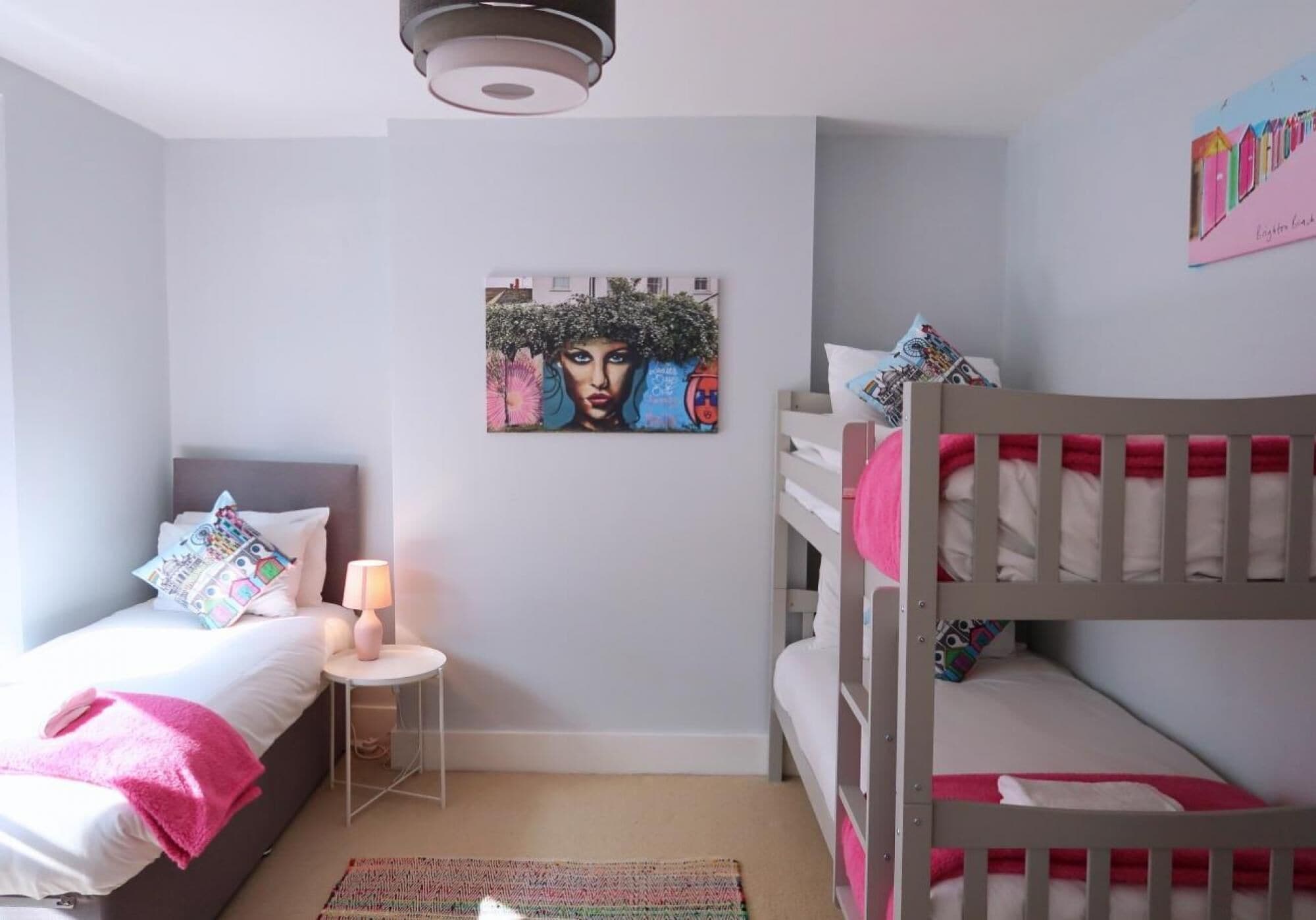A bedroom with a single bed, a nightstand, a lamp, a bunk bed, and a painting on the wall.