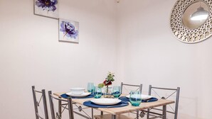 A dining area with a round table set for four, surrounded by metal chairs. There are blue glassware and a vase with a red flower on the table.