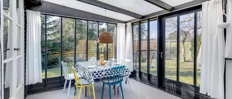 Relax in this serene sunroom with a garden view, featuring a round table and comfortable chairs.