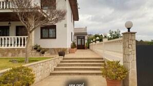 A two-story house with a stone facade, a balcony with a railing, and a staircase leading to the entrance. - RoomType (Rossell)