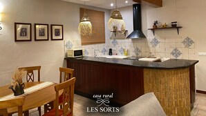 A kitchen with a central island, wooden chairs, a dining table, and a hanging light fixture. - RoomType (Rossell)