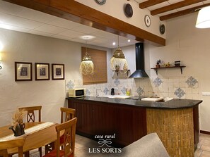A kitchen with a central island, wooden chairs, a dining table, and a hanging light fixture.