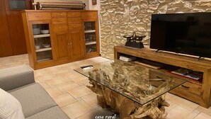 A living room with a glass coffee table, wooden cabinet, and a stone wall. - RoomType (Rossell)