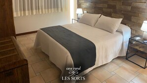 A bedroom with a stone wall, a bed with a black and white bedspread, a wooden headboard, and a nightstand with a lamp. - RoomType (Rossell)