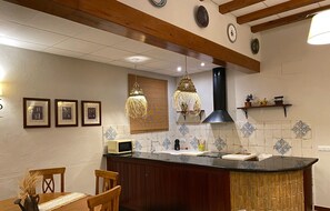 Una cocina con una isla central, sillas de madera, una mesa de comedor y una lámpara colgante.