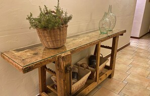 Una consola rústica de madera con cubierta de vidrio, cestas de mimbre y una planta en maceta.