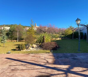Un patio empedrado con una farola, rodeado de árboles en flor y una zona ajardinada.