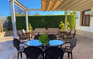 Un patio al aire libre con una mesa redonda de vidrio rodeada de sillas, un sofá a rayas y una planta en maceta.