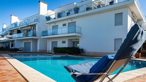 A modern apartment building with a swimming pool, a lounge chair, and a tiled patio.
