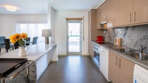 A modern kitchen with a marble countertop, stainless steel appliances, and a view to the outside.