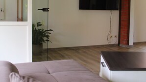 Una sala de estar moderna con un televisor de pantalla plana grande montado en la pared, piso de madera y una planta en maceta.