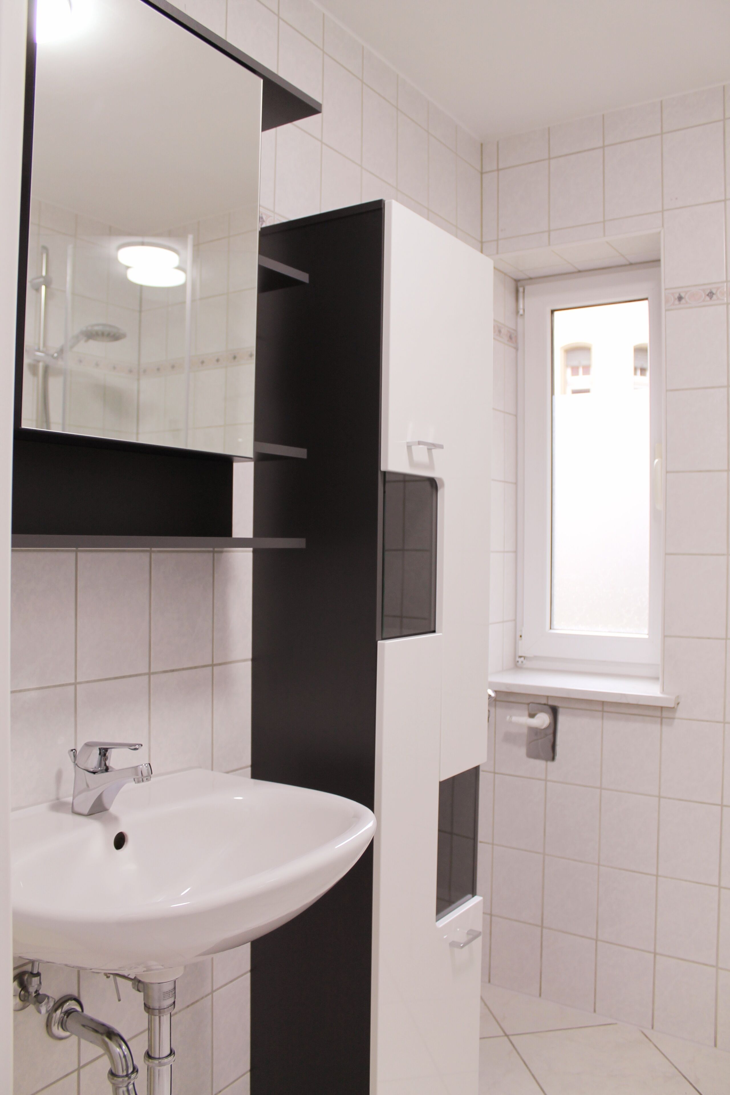 Une salle de bain avec un lavabo blanc, un miroir et une fenêtre.