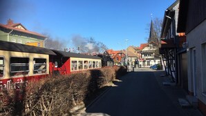 Una estación de tren con un tren detenido a la izquierda, edificios a la derecha y un cielo despejado.
