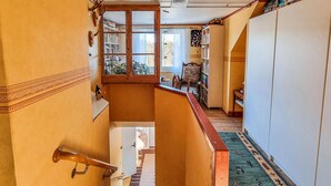 Un couloir étroit avec une rambarde en bois, une petite fenêtre et une porte donnant sur une autre pièce.