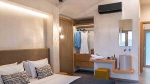 Habitación de hotel moderna con una cama grande, un vestidor amplio, un baño con espejo y lavamanos, y una lámpara colgante.