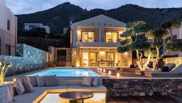 Una villa moderna con piscina, zona de estar exterior y un muro de piedra.