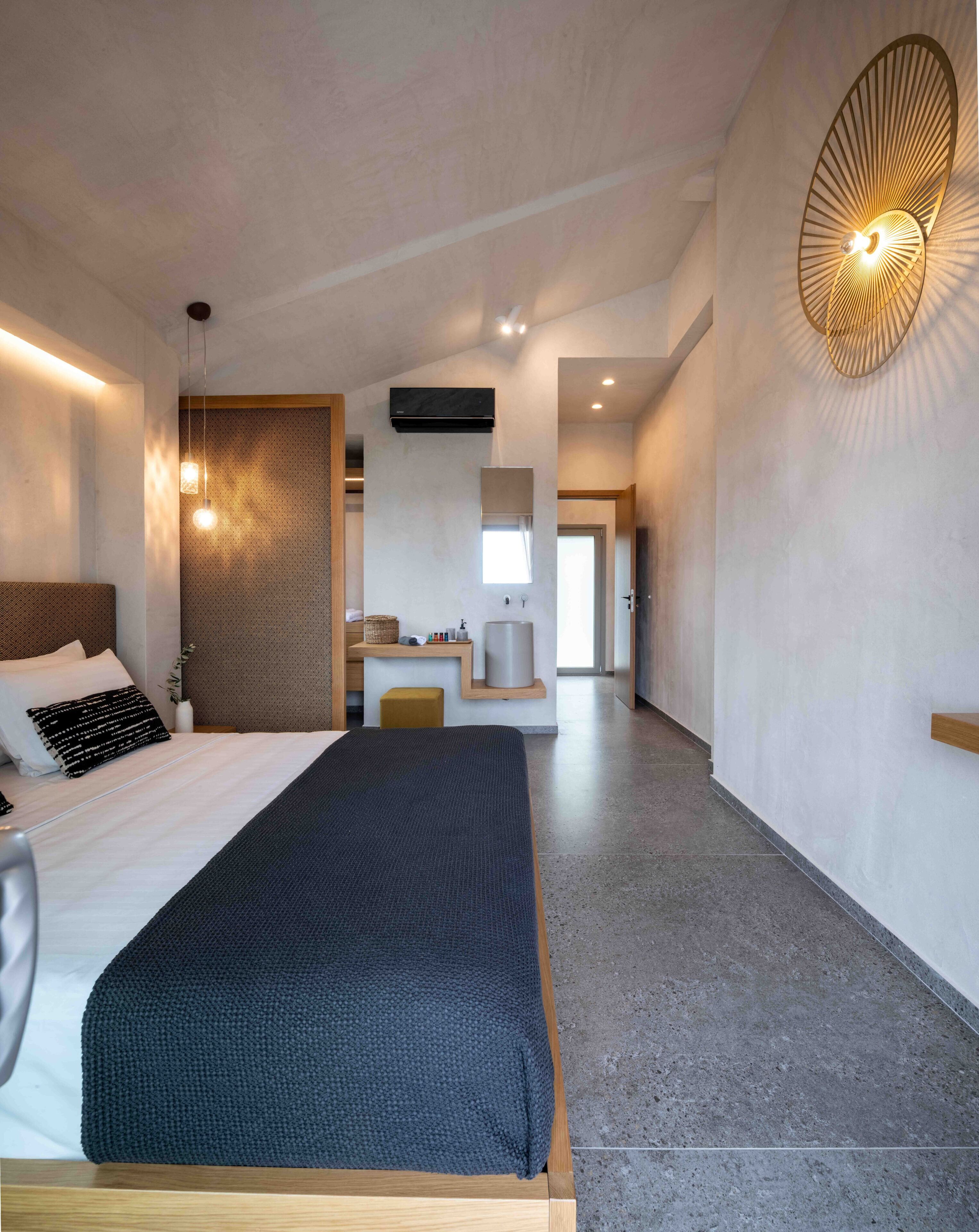A modern hotel room with a large bed, bedside tables, a vanity with a mirror, and a unique wall light fixture.