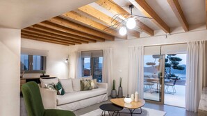 Una sala de estar moderna con techo de madera, un sillón verde, un sofá, una mesa de centro y vistas al exterior a través de amplios ventanales.