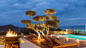 Un área junto a la piscina con sillones reclinables, una chimenea y vista al mar.