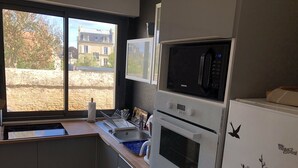 Cocina compacta con microondas, horno y refrigerador integrados. Una ventana ofrece vistas a un edificio y árboles.