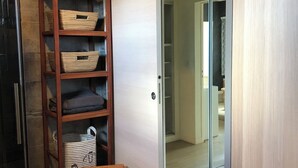Una habitación con puerta corredera de vidrio que da a un baño, una estantería de madera con cestas de almacenamiento y una pequeña mesa de madera.