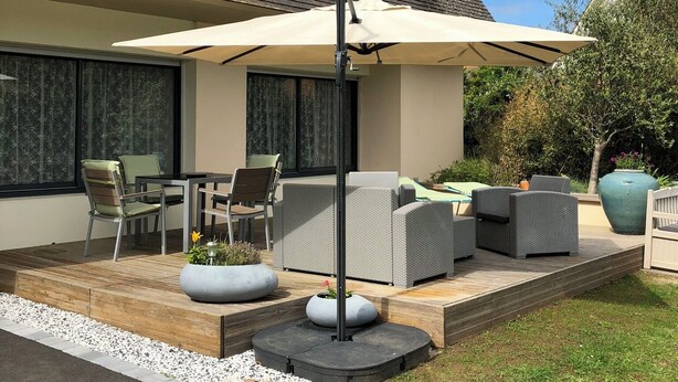 Una casa moderna con un patio amueblado al aire libre, un gran parasol y un jardín.
