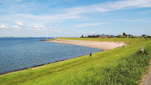 Een kustlandschap met een zandstrand, grasvelden en een gebouw met een rood dak.