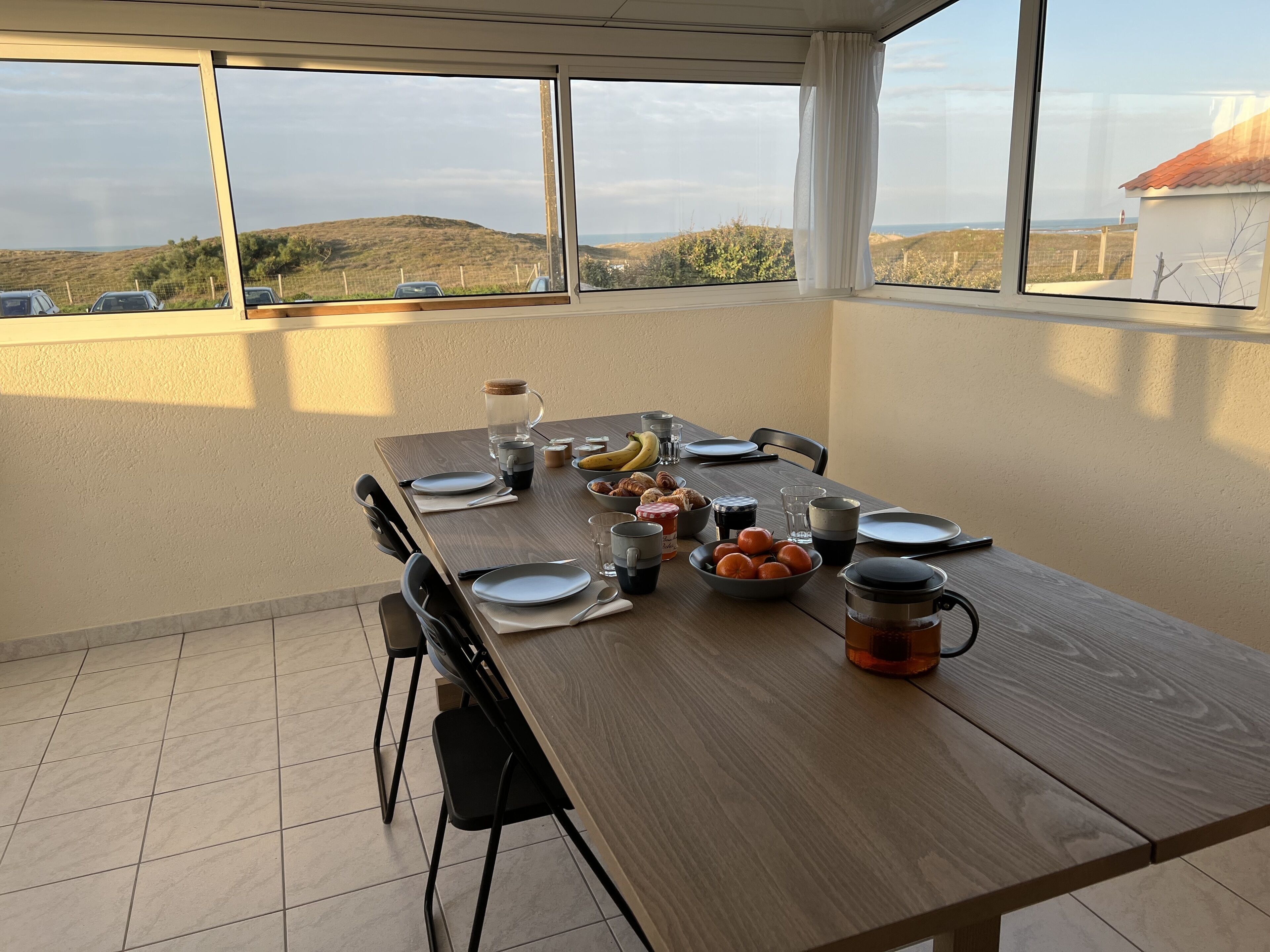 A dining table set with plates, bowls, and a pitcher, with a view of hills and a building in the background.