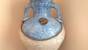 Una urna blu in ceramica con decorazioni elaborate e un dettaglio corda alla base, posata su un pavimento a disegno.