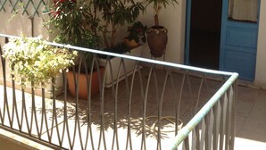 Un balcone con ringhiera metallica, piante in vaso, un estintore e una porta blu.