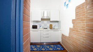 Una cucina compatta con mobili bianchi, un forno a microonde, un bollitore e un lavandino.
