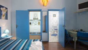 Una camera da letto con un letto, una scrivania, una sedia e un bagno parzialmente visibile attraverso una porta aperta.