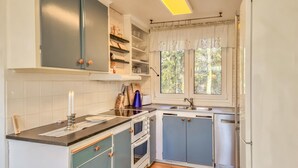 Une cuisine avec des meubles blancs, un plan de travail noir, une fenêtre avec des rideaux et un four encastré.