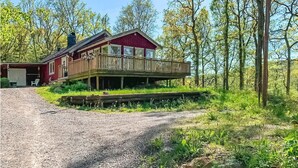 Une cabane rouge avec une terrasse en bois et une allée de gravier menant à un porche abrité.