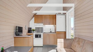 Una cocina funcional con armarios de madera, horno integrado, cafetera y televisor sobre una mesita.