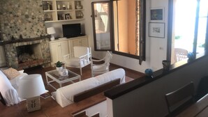 A living room with a stone fireplace, white furniture, a television, and a large mirror. - Panoramic villa on the sea Villasimius (Villasimius)