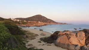 A coastal landscape with a sandy beach, rocky outcrops, and a hill with buildings in the background. - Panoramic villa on the sea Villasimius (Villasimius)
