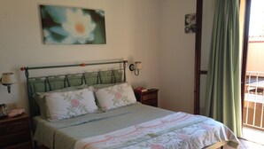 A bedroom with a bed, a nightstand, a wall-mounted lamp, and a window with curtains. - Panoramic villa on the sea Villasimius (Villasimius)