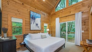 A wooden cabin bedroom with a bed, nightstands, a poster, and a sliding glass door to a deck. - Range Views - 2 BR w/Sleep Loft, Hot Tub, Firepit at Maggie Valley Club (Maggie Valley)
