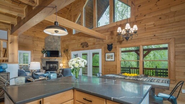 A wooden cabin interior with a kitchen island, dining area, and large windows. - Range Views - 2 BR w/Sleep Loft, Hot Tub, Firepit at Maggie Valley Club (Maggie Valley)