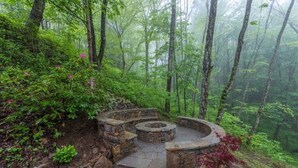 A stone-built circular seating area surrounded by forest. - Range Views - 2 BR w/Sleep Loft, Hot Tub, Firepit at Maggie Valley Club (Maggie Valley)
