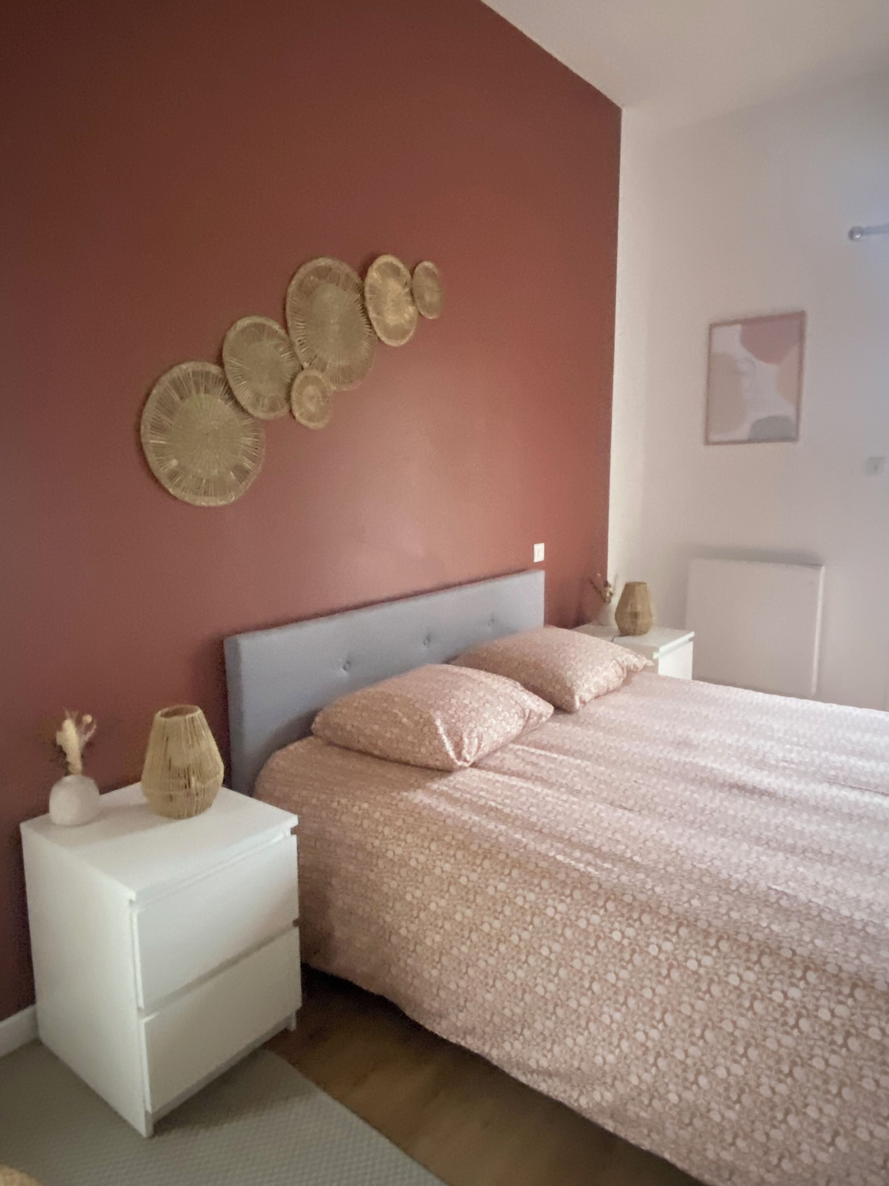 Une chambre à coucher comprenant un lit, des tables de chevet, une lampe fixée au mur et un élément décoratif mural.