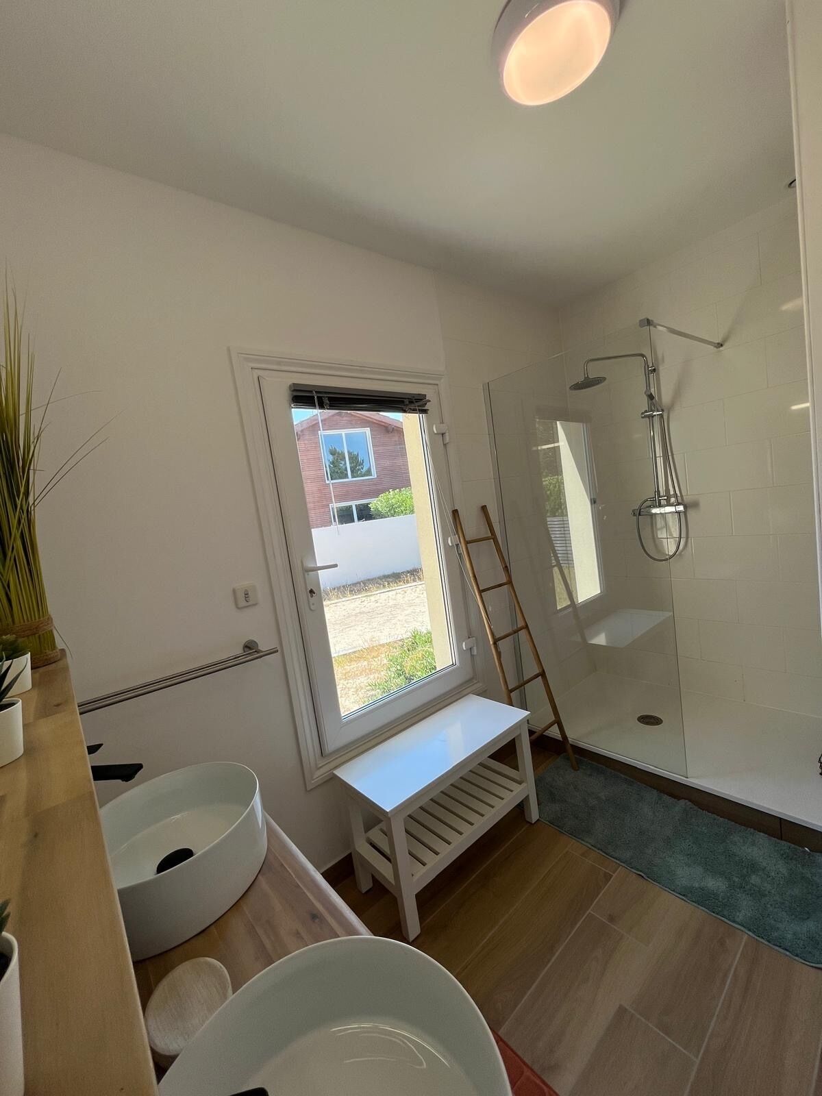 A modern bathroom with a glass shower enclosure, a white sink, and a window providing natural light.