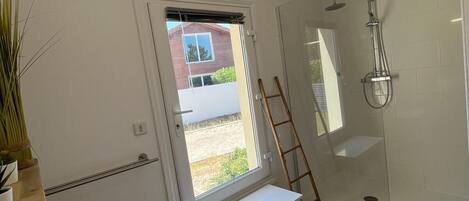 A modern bathroom with a glass shower enclosure, a white sink, and a window providing natural light.